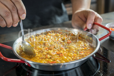 Chef is cooking paella with spoon, close up