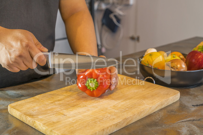 Chef cutting red bell pepper on wooden broad