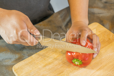 Chef cutting red bell pepper on wooden broad