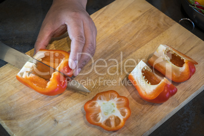 Chef cutting red bell pepper on wooden broad