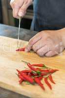 Hand slicing Chilli pepper with Knife on chopping board on woode