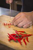 Hand slicing Chilli pepper with Knife on chopping board on woode