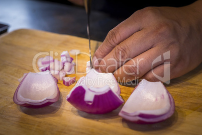 Chef chopping a red onion with a knife on the cutting board