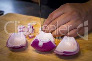 Chef chopping a red onion with a knife on the cutting board