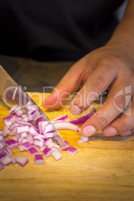 Chef chopping a red onion with a knife on the cutting board