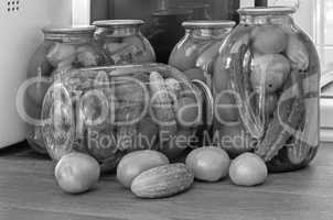 Canned tomatoes and cucumbers in large glass jars. Black-and-white image.