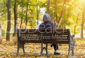 Elderly woman sitting on a bench in autumn park