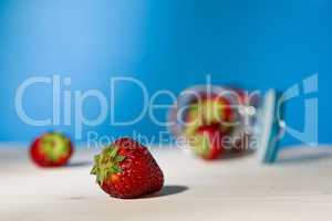 Close up of a strawberry and a glass jar full of strawberries lying down on a table