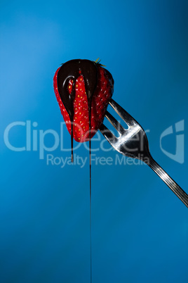 Close up of a strawberry suspended from a fork with liquid choco