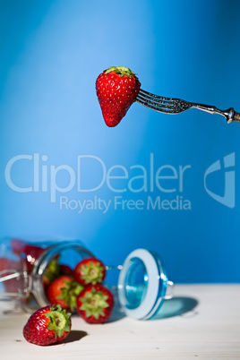 Strawberry suspended from a fork and under a jar of strawberries