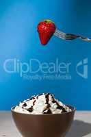 Strawberry suspended from a fork over a cup of whipped cream and