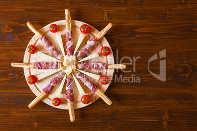 Chopping board with ham rolled in breadsticks cheese and cherry