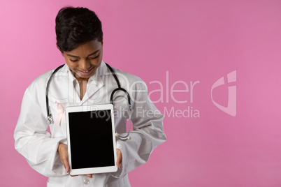 Smiling nurse wearing breast cancer awareness pink ribbon looks at her tablet