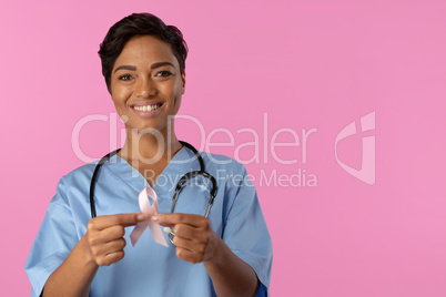 Smiling nurse holding breast cancer awareness pink ribbon with both hands