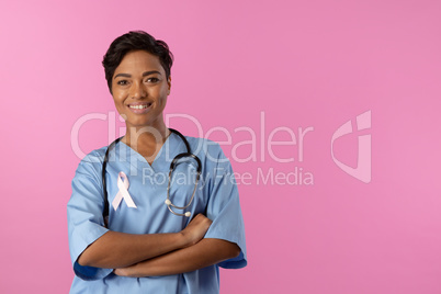 smiling nurse with crossed arms wearing pink ribbon