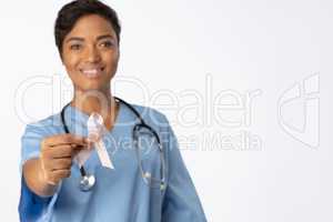 Smiling nurse holding breast cancer awareness pink ribbon between her fingers