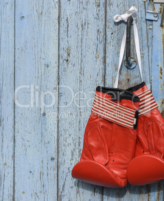 red leather boxing gloves hanging on an old blue wooden wall