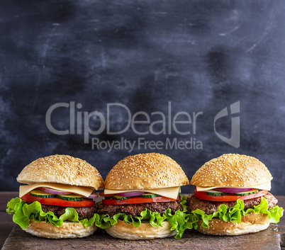 three hamburgers with vegetables on a brown wooden board