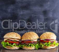 three hamburgers with vegetables on a brown wooden board