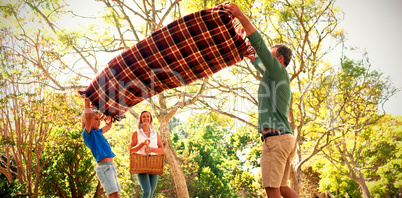 Father and son spreading the picnic blanket while mother carrying basket