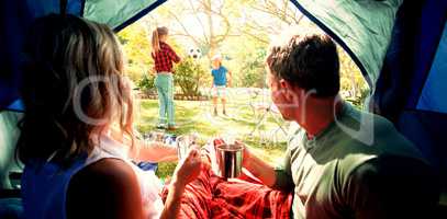 Couple having coffee and looking at kids playing outside the tent