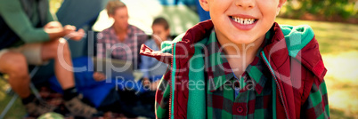 Boy smiling at camera while family sitting at tent in background