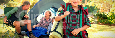 Boy holding a rolled mat while family sitting in the tent