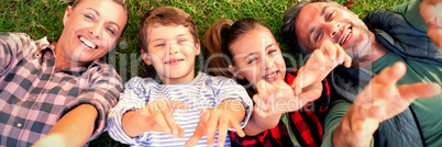 Happy family lying on the grass and making hand gestures