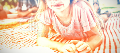 Girl lying on blanket and reading book while family sitting in background