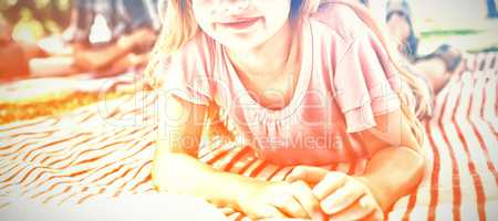 Girl lying on blanket and reading book while family sitting in background