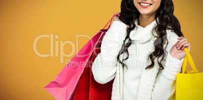 Composite image of smiling woman with christmas hat holding colored shopping bags