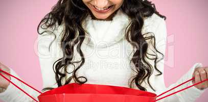 Composite image of happy woman with christmas hat looking in red shopping bag