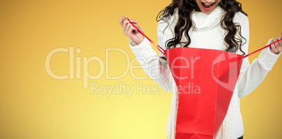 Composite image of surprised woman with christmas hat looking in red shopping bag