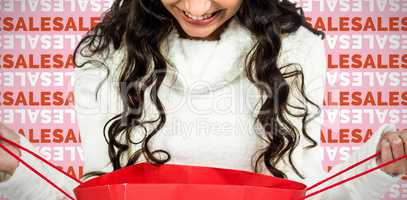 Composite image of happy woman with christmas hat looking in red shopping bag