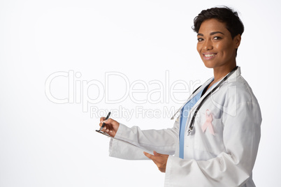 Smiling female doctor wearing breast cancer awareness pink ribbon writing on a note pad