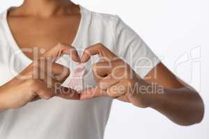 Women making heart with their fingers around pink ribbon