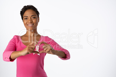 Smiling women wearing pink shirt making heart with their fingers around pink ribbon