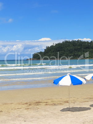 View of the beach with umbrella, waves and island.