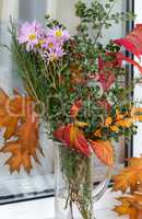 Bouquet of autumn flowers and leaves on the windowsill.