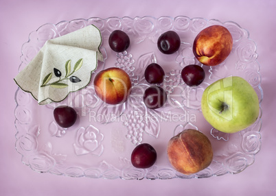 Plums, peaches, apples on a glass tray.