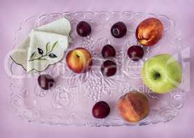 Plums, peaches, apples on a glass tray.
