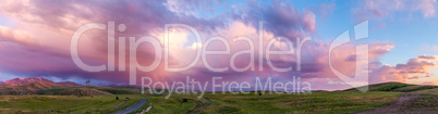 Panorama of a mountain valley at sunset with bright pink clouds and a red rainbow