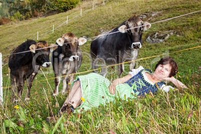 Woman in dirndl is before their cows in the grass