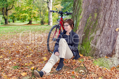 Woman with bicycle sitting in the leaves in autumnal park