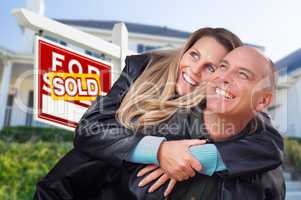 Happy Couple Hugging in Front of Sold Real Estate Sign and House