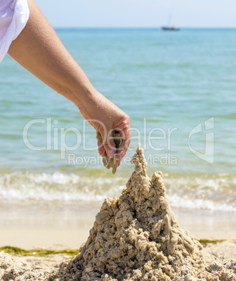 hand builds a castle from the wet sea sand