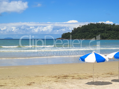 View of beach with parasol and island in the background.
