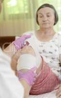 Doctor bandaging senior woman leg at home