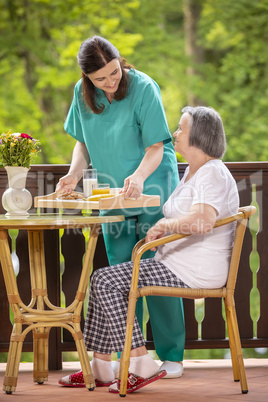 Nurse serving healthy breakfast to happy senior woman