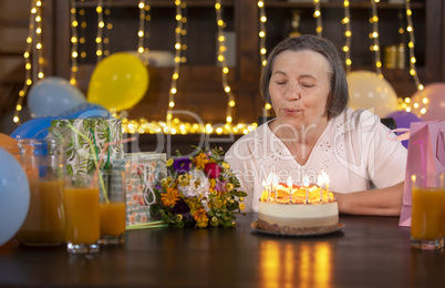 Elderly woman blowing candles at her birthday celebration